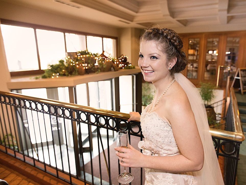 A bride smiling while she sips champagne overlooking the entrance to the building